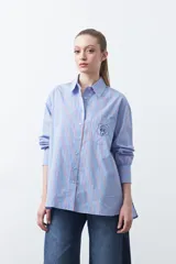 Camisa a rayas verticales blancas y marrones, de manga larga con puños abotonados, cuello camisero y botones frontales. Incluye un bolsillo en el pecho con bordado sutil.