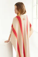 Ruana artesanal de tejido de punto, color beige con franjas horizontales gruesas rojas y finas amarillas. Posee flecos en el borde inferior.