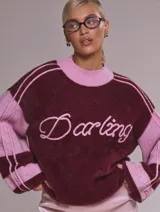 Sweater oversize de punto suave en combinación bicolor bordó y rosa, con cuello redondo tejido y estampa frontal con la palabra Darling en tipografía cursiva.