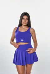 Conjunto deportivo compuesto por un top corto de escote redondo con logo estampado y una pollera short con vuelo. Ambas piezas son de color violeta.