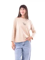 Remera de manga larga color beige claro, con cuello redondo y un pequeño bordado frontal de un perro con rayas.