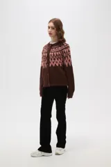 Cardigan de tejido jacquard con diseño geométrico en la parte superior, cuello redondo y cierre frontal con botones. Presenta un corte holgado y mangas largas con puños acanalados.