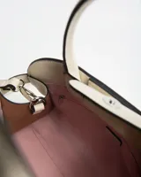 Cartera tipo bolso de mano color beige, confeccionada en símil cuero, con doble asa corta y detalles de tiras laterales decorativas con hebillas. Incluye correa ajustable y el logotipo de la marca impreso en metal en la parte inferior frontal.