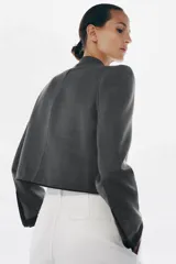 Blazer de corte cropped confeccionado en tejido de lana gris, con cuello redondo y cierre frontal mediante alamares decorativos. Presenta bolsillos delanteros con solapa y puños a contraste en color negro.