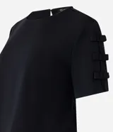 Blusa de crepé color negro, con cuello redondo, cierre tipo gota en la espalda y mangas cortas decoradas con apliques de lazos laterales.
