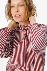 Camisa de manga larga con estampado de rayas verticales en color bordó y blanco. Presenta un cuello alto con volados y cierre frontal con botones a tono.