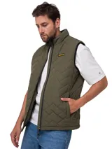 Chaleco matelaseado de color verde militar, con cuello alto, cierre frontal con cremallera y bolsillos laterales con cierre. Cuenta con un parche de la marca Caterpillar en el pecho y ribetes elásticos.