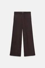 Pantalón de tiro bajo y corte recto, color marrón oscuro. Presenta bolsillos laterales, cierre frontal con cremallera y gancho metálico, y un cinturón integrado del mismo tejido con hebilla metálica.