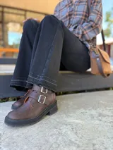 Botas cortas de cuero color marrón con suela track negra. Presentan dos correas ajustables con hebillas metálicas plateadas en el empeine y cierre lateral interno.