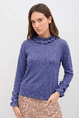 Polera de manga larga color azul jaspeado, con cuello alto y puños decorados con volados. Presenta un calce cómodo y relajado.