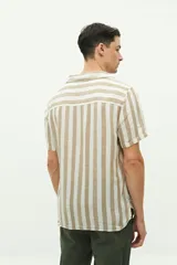 Camisa de manga corta con cuello cubano, confeccionada en una mezcla de lino y algodón con textura. Presenta un diseño a rayas verticales en tonos beige y celeste sobre fondo blanco, con cierre frontal de botones y logo bordado en el pecho.