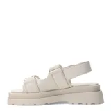 Sandalias chunky de color marfil con plataforma y suela dentada. Presentan dos tiras frontales anchas con cierre de velcro decoradas con pequeños tachas doradas, y una tira trasera ajustable.