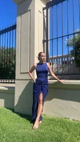 Vestido largo de fiesta color azul noche, con escote redondo y diseño ajustado en el torso. Presenta un detalle de nudo frontal en la cintura que da paso a una falda con abertura lateral y caída fluida.