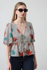 Blusa de silueta relajada con estampado de rayas verticales y motivos florales en tonos naranja y turquesa. Presenta escote en V con lazos frontales regulables, mangas cortas con leve volumen y detalle de frunce bajo el busto que aporta movimiento.