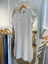 Vestido midi azul marino de lino, corte recto, con cuello en V, mangas cortas y detalle de flecos en ruedo y mangas.