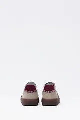 Zapatilla urbana de mujer con base de goma marrón, capellada en beige y blanco, y detalles bordados en color bordó. Cierre con cordones bordó.