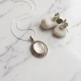 Dije ovalado de acero con centro de nácar y borde texturizado, incluye cadena fina de acero.