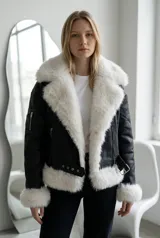 Campera tipo gamulán de ecocuero negro con interior y detalles de piel sintética blanca en cuello, puños y ruedo. Presenta cierre frontal, cinturón ajustable en la cintura y bolsillo con cierre en la manga.