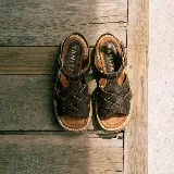 Sandalias de cuero vacuno negro con textura símil cocodrilo, diseño de tiras cruzadas, suela track de goma y hebilla metálica de ajuste en el tobillo.