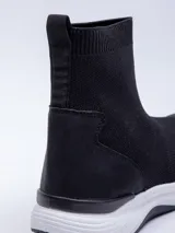 Zapatilla negra de textil elastizado, de caña media y calce tipo media. Detalle de pieza de PU en el talón.