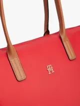 Cartera tote Tommy Hilfiger de nailon rojo, con cierre de cremallera, asas superiores de cuero sintético tostado y monograma metálico TH en la parte delantera.