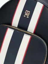 Mochila urbana de diseño estructurado en color azul marino, con franjas verticales en blanco y rojo en el centro. Presenta el logo monograma TH metalizado en la parte superior, bolsillo frontal con cierre y herrajes dorados.