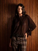 Blusa de plumeti color marrón, con cuello alto ajustable mediante lazo, mangas largas con puños con volados y diseño holgado.