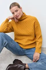 Polera de tejido de punto color ocre con cuello alto, diseño de rombos en relieve en el frente y mangas con detalle de trenzas laterales.