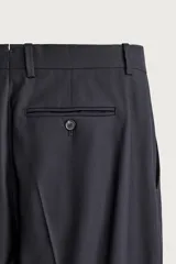 Pantalón de traje relaxed fit color negro, confeccionado en tejido con lana, con bolsillos frontales, bolsillos traseros de doble vivo con botón y raya marcada en las piernas.