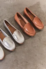 Mocasines de cuero color dorado con acabado texturizado, diseño clásico de punta redondeada y costuras visibles en el empeine. Cuentan con suela plana y flexible.