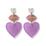 Par de aros colgantes con forma de corazón y labios. El dije superior es un corazón plateado con glitter, seguido por un dije con forma de labios color rosa pálido y un dije inferior con forma de corazón lila con glitter.