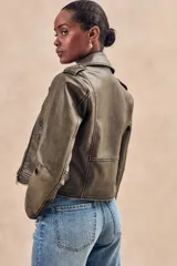 Campera corta color verde oliva de cuero sintético con cuello clásico, cierre frontal asimétrico con cremallera, bolsillos con cremallera y solapa, y detalles de costuras en los hombros.