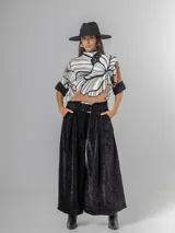 Pantalón tipo palazzo de corte oversized, confeccionado en tela con textura aterciopelada en color negro. Presenta cintura alta con pinzas, bolsillos laterales y un cinturón ancho integrado con hebilla al tono.