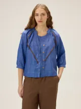 Camisa azul de lino con mangas 3/4, cuello redondo y detalles de ribetes en contraste.