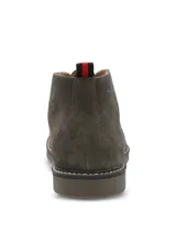 Botines tipo chukka Hush Puppies modelo New Safari, confeccionados en gamuza color gris. Presentan cierre de cordones, suela de goma con costura decorativa y detalle de tirador en el talón con franjas rojas y negras.