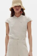Camisa de lino color beige, con cuello mao y cierre cruzado al costado mediante botones de nácar. Presenta mangas cortas y diseño entallado.