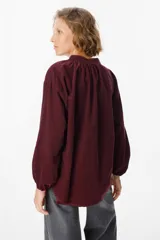 Camisa de pana color verde oliva, con cuello mao, cierre frontal de botones y mangas largas abullonadas con puños elásticos.