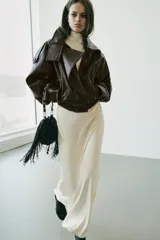 Bolso tipo saca color negro, de formato mini, con flecos laterales, cierre fruncido con cordones y correa combinada de cadena y tira de cuero sintético.