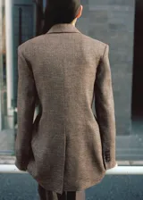 Blazer de corte recto y cruzado color marrón jaspeado, confeccionado en mezcla de lino. Presenta cuello pico con solapa de muesca, cierre delantero de un botón y dos bolsillos con solapa en los laterales.