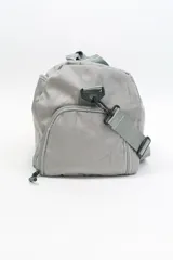 Bolso de viaje gris con doble asa corta y cierre superior. Estampado frontal con la frase "The Tote Bag" en letras blancas.