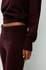 Buzo de punto fino color bordó, con escote off-the-shoulder y hombros caídos. Tiene mangas largas y remate acanalado en puños y bajo.