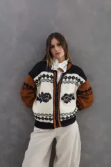 Campera bomber tejida de 100% lana merino con diseño multicolor en tonos negro, blanco y marrón, con cierre frontal y detalles de guardas patagónicas y flores.
