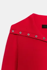 Chaqueta de punto color rojo, con cuello solapa y manga larga. Cierre frontal con fila de botones negros en contraste que se extienden también sobre el cuello.
