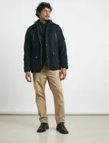 Campera de abrigo color verde militar, con capucha desmontable forrada, cierre frontal con cremallera y botones a presión. Cuenta con múltiples bolsillos: dos en el pecho con cierre, dos en la cintura con botones y un bolsillo en la manga. El interior está forrado para mayor calidez.