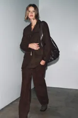 Blazer de mujer color marrón oscuro, confeccionado en piel de ante 100%. Presenta cuello solapa de muescas, manga larga, bolsillos de plastrón frontales y cierre frontal de botones.