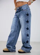 Jean de tiro medio con corte recto y holgado, confeccionado en denim azul. Presenta un diseño con estrellas bordadas en color oscuro a lo largo de las costuras laterales.