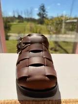 Sueco marrón de cuero trenzado con hebillas plateadas y suela de goma negra.