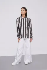 Camisa de manga larga con cuello clásico y cierre frontal de botones. Presenta un estampado de rayas verticales irregulares en tonos oscuros, blancos y verde claro.