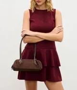 Cartera tipo shoulder bag de tamaño pequeño y formato alargado, confeccionada en material sintético efecto gamuza. Cuenta con asas de hombro estructuradas, cierre superior con cremallera y detalles metálicos decorativos.