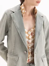 Blazer de denim color gris con lavado gastado, solapas clásicas, cierre frontal de un botón y bolsillos con tapa.